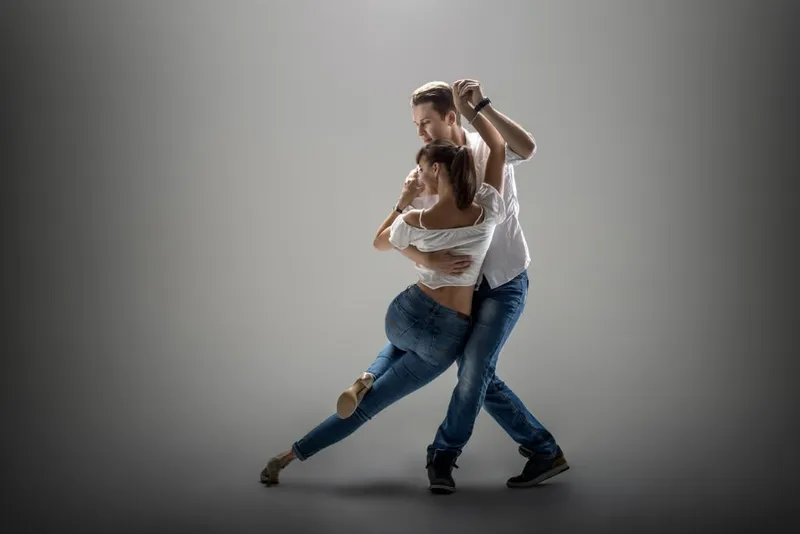 A couple in a stretched dance pose against a grey backdrop