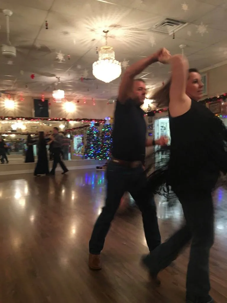A couple dancing in a large ballroom lit with string lights